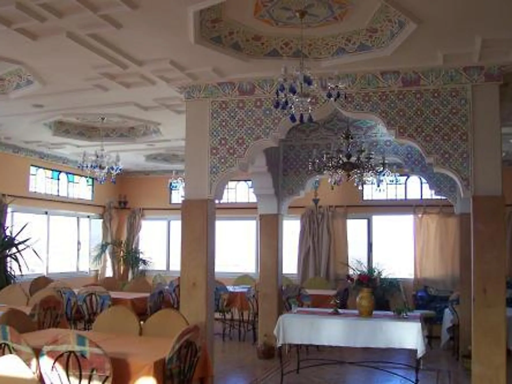Le salon de la maison, arcade sculptée, plafonds peints et tables dressées près des fenêtres.