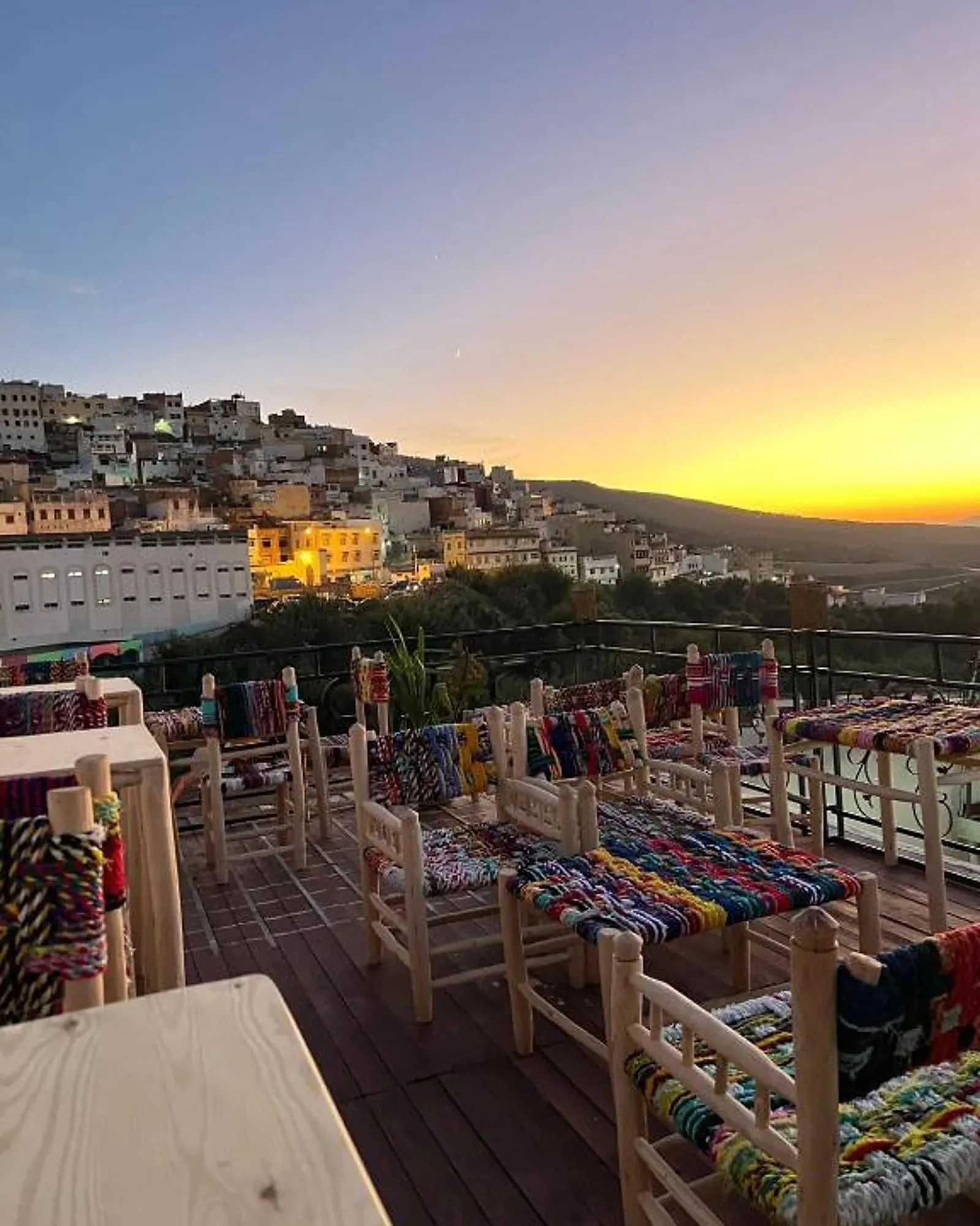 La terrasse au crépuscule, chaises tissées face à la ville illuminée et au massif du Zerhoun.